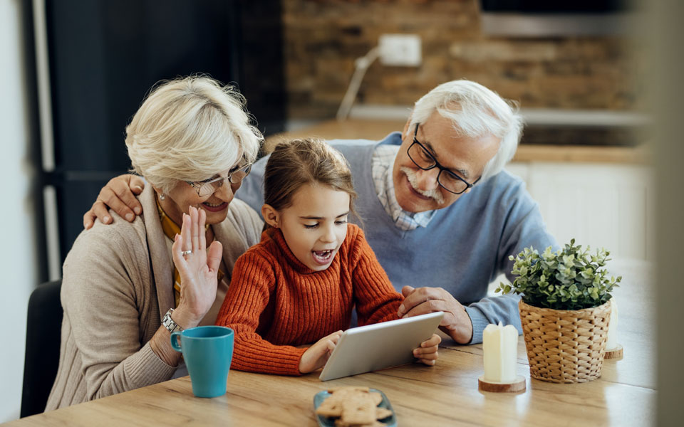 Deux couples de seniors et leur petite-fille en appel vidéo sur une tablette.