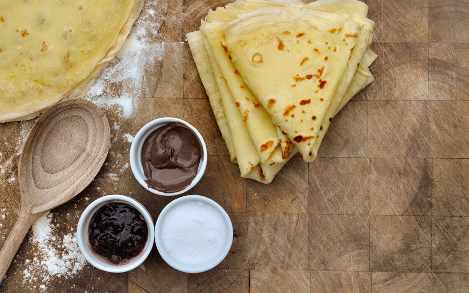 Ingrédients pour crêpes disposés sur une table en bois, incluant farine, œufs, lait et beurre.